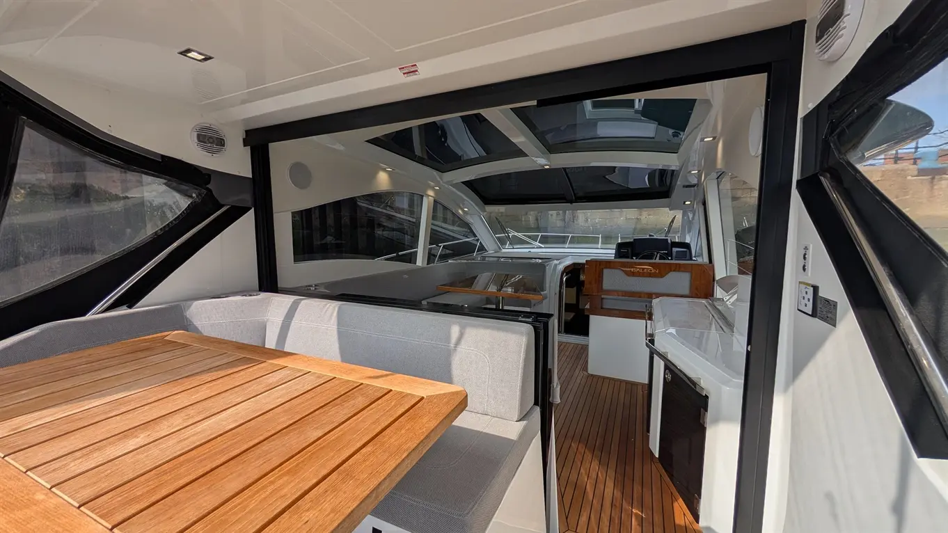 Interior of a modern boat featuring a wooden table, grey seating, and a fully equipped galley with a window view.